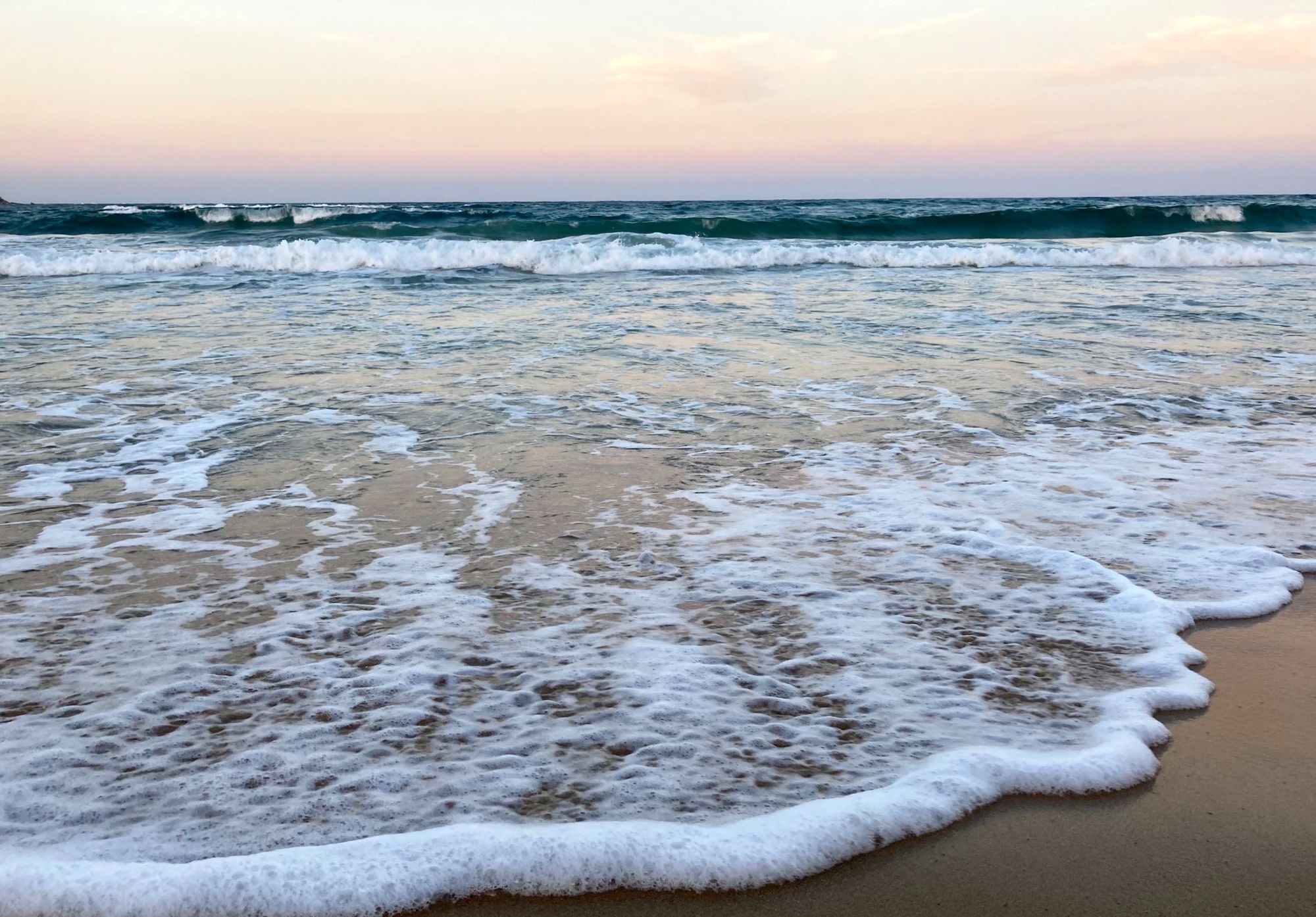 Sea foam on sand under a soft pink horizon
