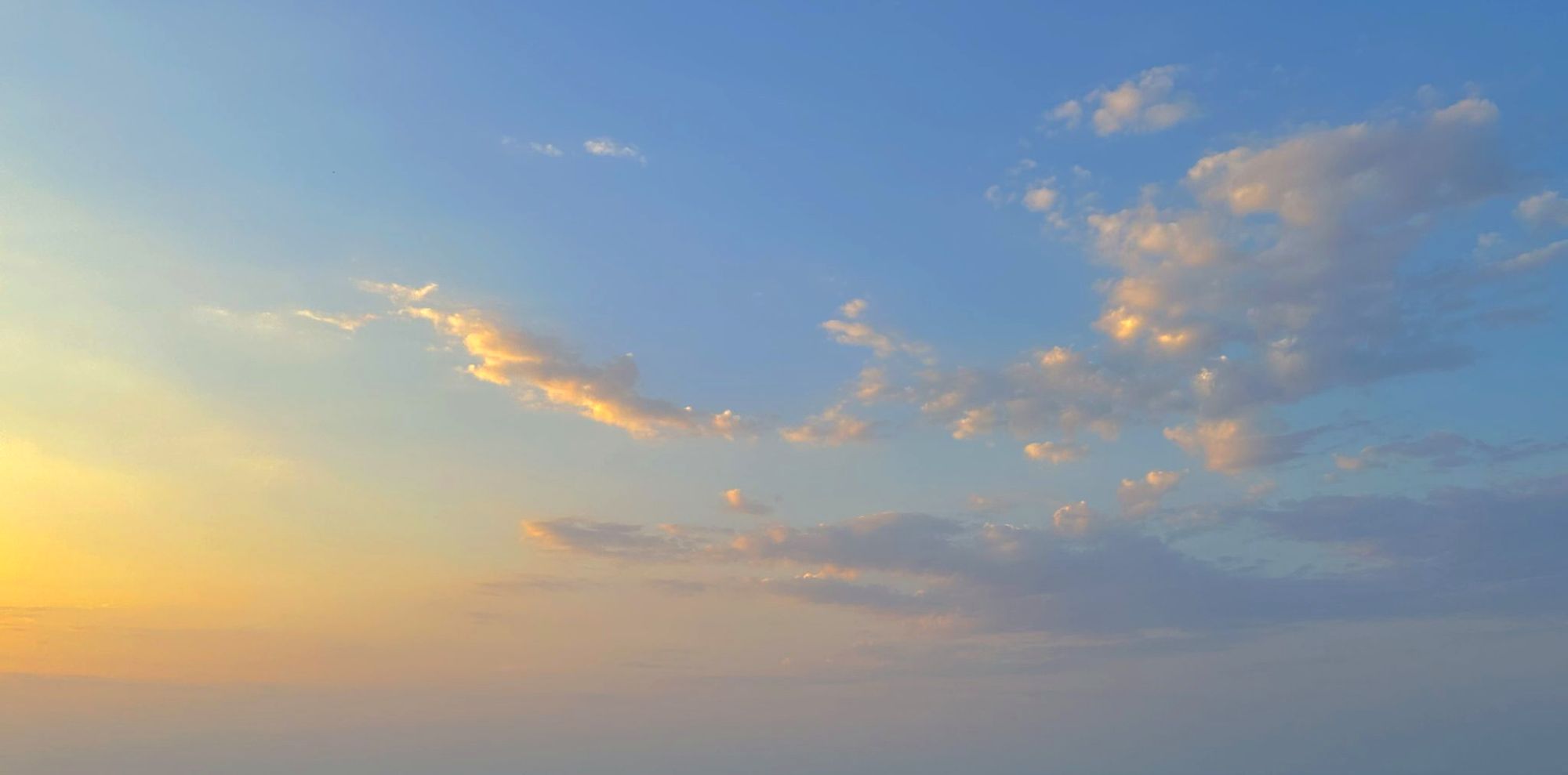 Blue evening sky with gold-lit clouds over the sea