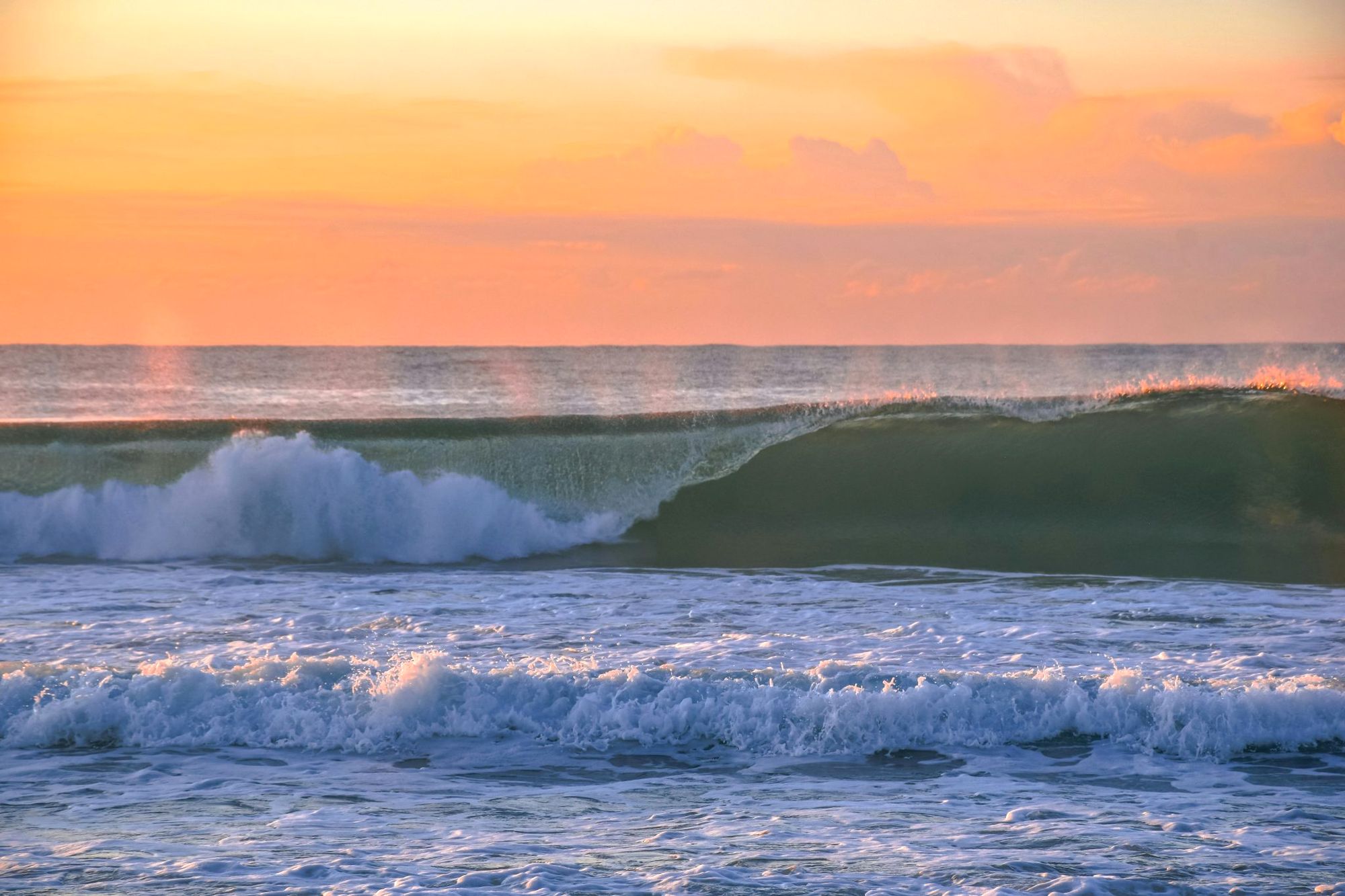 A turquoise wave under a peach sky