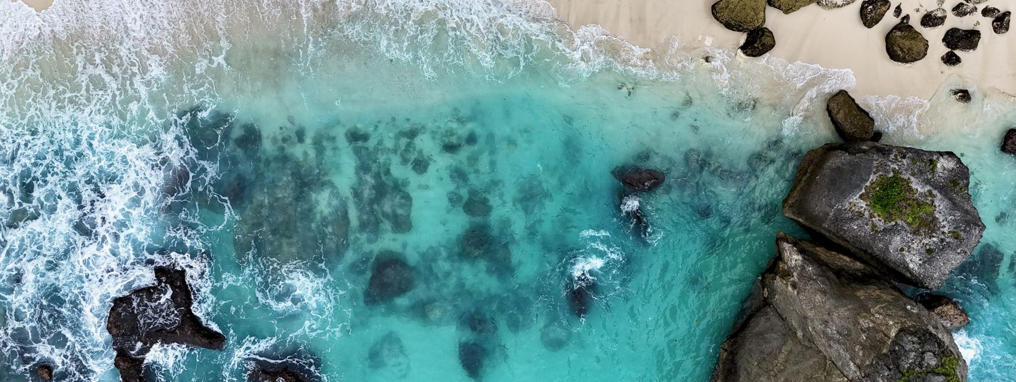 Turquoise surf over sand and rocks, from above